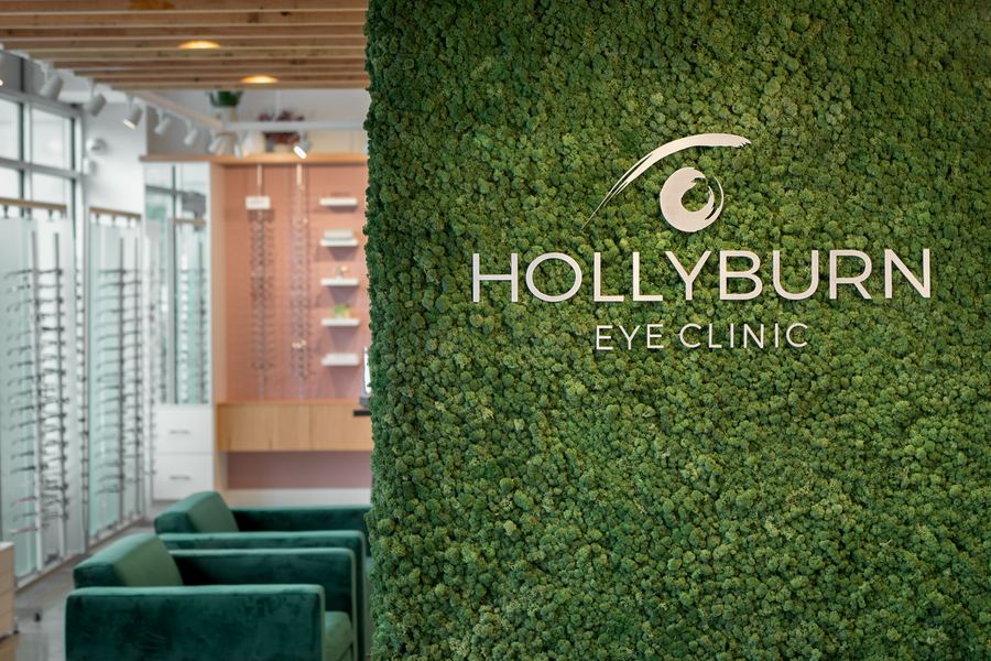 Hollyburn Eye Clinic — full retail floor with green velvet seating, moss wall column and floor-to-ceiling windows overlooking Lonsdale Quay